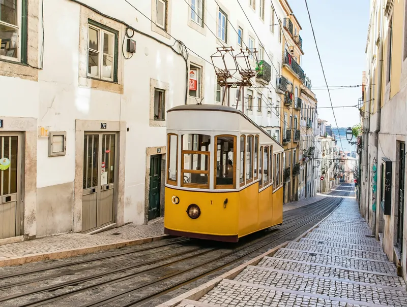 Знаменитый фуникулер Бика (Elevador da Bica) в Лиссабоне, старинный желтый вагончик, поднимающийся по крутой улице.